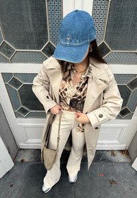 Beige trench coat egy barna és krémszínű mintás ing felett, krémszínű kordbársony trapéz nadrág, farmer sapka és egy kicsi bézs kézitáska.