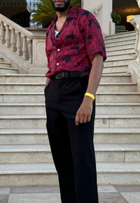 Röd och svart mönstrad kortärmad skjorta som matchas med svarta byxor, med ett bälte och en synlig ficka för tillbehör. Gul handledsrem närvarande.