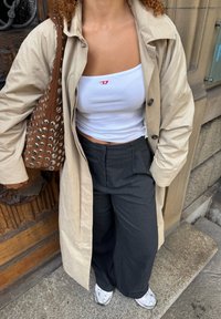 Beige trench coat, valkoinen ribattava crop-top punaisella logolla, harmaat leveälahkeiset housut, ruskea niittilaukku, hopeiset lenkkarit.