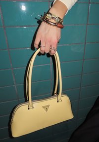 Kollane nahast käekott ümmarguse kujuga, kahekordsete käepidemetega ja hõbedaste detailidega. Omab nähtavat logo ja tõmbluku detaile.