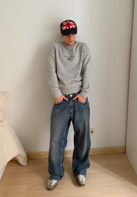 Šedá mikina s logem, oversized modré džíny a šedé tenisky. Baseballová čepice má design Union Jack v červené a bílé barvě.