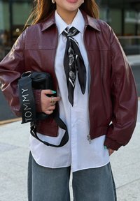 Burgundi bőr bomber dzseki bordázott mandzsettákkal és ezüst cipzárral. Fehér ing és fekete mintás sál. Fekete táska "TOMMY" pánttal.