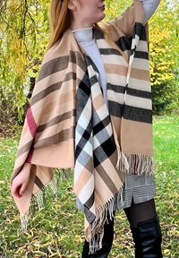 Châle à carreaux aux couleurs beige, noir et blanc avec des bords frangés. Porté drapé sur les épaules, mettant en valeur des motifs à carreaux audacieux.