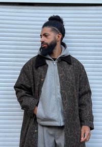 Manteau imprimé léopard marron avec un col en velours côtelé, superposé à un sweat à capuche gris clair à fermeture éclair et un pantalon de survêtement assorti. Texture lisse, coupe décontractée.
