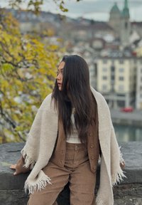 Pantalon en velours côtelé marron chaud assorti à un châle crème à franges et un cardigan marron à boutons. Cheveux longs bruns et toile de fond naturelle en plein air.