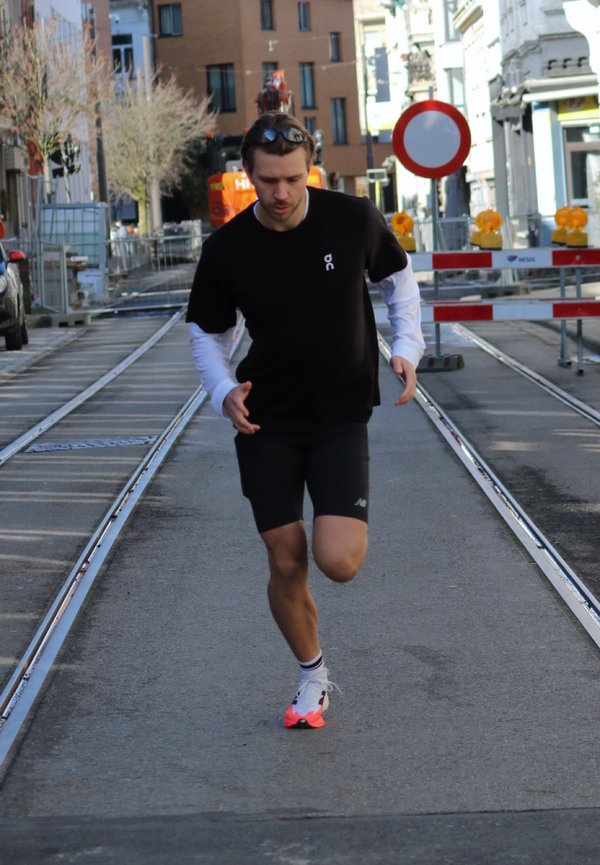 Mann in schwarzer Kleidung, der auf einer gepflasterten Straße mit Straßenbahnschienen läuft, in der Nähe von Straßensperren und einem Durchfahrtsverbotsschild.