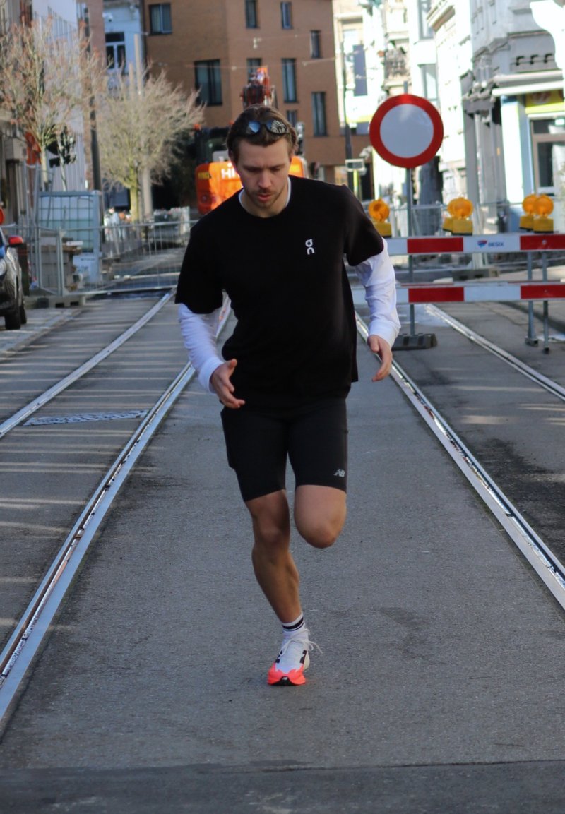 Muž oblečený v čiernom, ktorý beží po asfaltovej ulici s koľajnicami pre električku, v blízkosti cestných stavebných zábran a dopravnej značky zákaz vstupu.