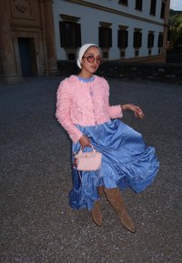 Ρυθμισμένο ροζ κοντό σακάκι πάνω από ένα μπλε σατέν φόρεμα με φουσκωτές λεπτομέρειες. Τα αξεσουάρ περιλαμβάνουν μια μικρή ροζ τσάντα και μπεζ μπότες ως το γόνατο.