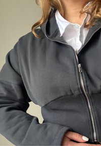 Hall hall lukuga dressipusade soonikkoes ääre ja varrukatega. Omab kõrget kraed ja sileda tekstuuriga kangast, kantud valge särgi peal.