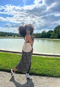 Weißes und schwarzes blumenmuster Maxikleid mit geflochtenem Oberteil. Person trägt weiße Sneakers. Vor einem Teich und grünem Landschaftshintergrund unter einem blauen Himmel.