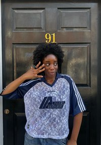 Marineblå Adidas-trøye med blondeoverlay, med hvite striper på ermene og logo. Personen har på seg en stor svart ring og denimjeans.