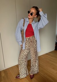 Prugasta košulja na dugih rukava, crni top, široke hlače s leopard uzorkom, crne sunčane naočale i crvene štikle u zatvorenom prostoru.