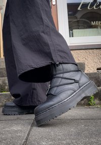 Bottines en cuir noir avec une finition texturée, bout arrondi et semelle en caoutchouc épaisse avec un motif en zigzag. Fermeture à lacets et à glissière.