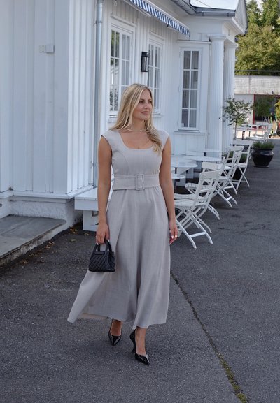 Mono sin mangas gris claro con un escote amplio, cintura ceñida y patas acampanadas; combinado con un bolso negro acolchado y tacones de punta.