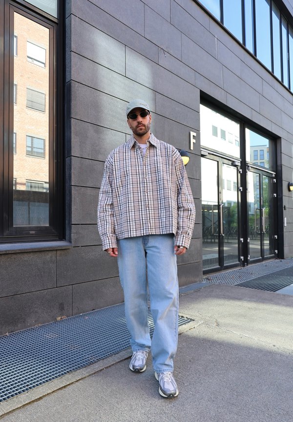 Oversized beige and checkered flannel shirt, light blue jeans, grey sneakers with white details, and a light cap. Dark sunglasses.