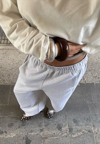 Világosszürke melegítőnadrág, elasztikus derékkal, sötét pöttyös slip-on cipővel párosítva. Egy bézs színű, hosszú ujjú felső és karkötők láthatók.