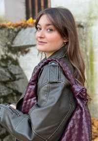 Veste en cuir noir avec un sac tressé bordeaux. La veste présente une poche zippée et des épaules structurées. Texture douce et lisse visible.