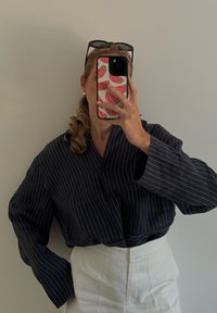 Námornícky modrá košeľa s prúžkami a uvoľneným strihom, dlhé rukávy, cez biele nohavice s vysokým pásom, minimalistický dizajn, hladká textúra látky.
