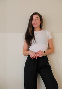 Hvit skjorte tilpasset kroppen, kombinert med svarte løse bukser, accessorert med lagde armbånd og et klokke, foran en nøytral vegg.