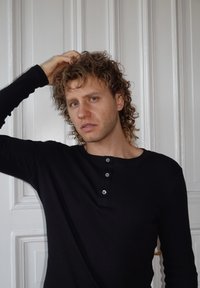 Maglietta nera a maniche lunghe con scollo arrotondato e tre bottoni sul petto, con una texture a costine. Sfondo bianco.