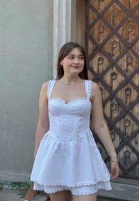 Weißes Baumwollkleid mit tailliertem Oberteil und Spitze, einem ausgestellt Rock und aufwendiger Stickerei, ergänzt durch einen mehrlagigen Saum.