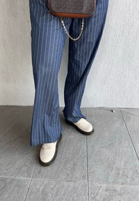 Pantalons larges à rayures bleues, en tissu léger, associés à des chaussures à enfiler de couleur crème avec des semelles noires et des coutures jaunes.