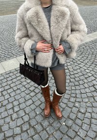 Faux fur grå jakke med brede slag, strikket grå sweater, grå shorts, sort læderhåndtaske og brune knæhøje støvler med hvide detaljer.