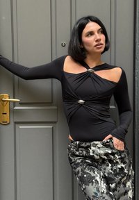 Zwart lang mouwen bodysuit met open schouders en een gedraaide ontwerp, geaccentueerd met zilveren hardware, gecombineerd met zwart-grijze broek met patroon.