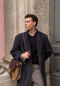 Garšīgs tumšs mētelis ar teksturētu apdari, melna džemperis zem tā un beid�ža krāsas bikses. Brūna soma ar ādas akcentiem, kuru tur ar vienu roku.