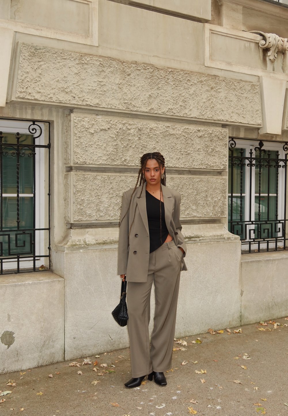 Blazer gris a medida y pantalones de pierna ancha, combinados con un top negro y bolso. Tela suave con textura sutil, ambientados en un fondo urbano.