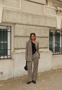 Blazer gris a medida y pantalones de pierna ancha, combinados con un top negro y bolso. Tela suave con textura sutil, ambientados en un fondo urbano.