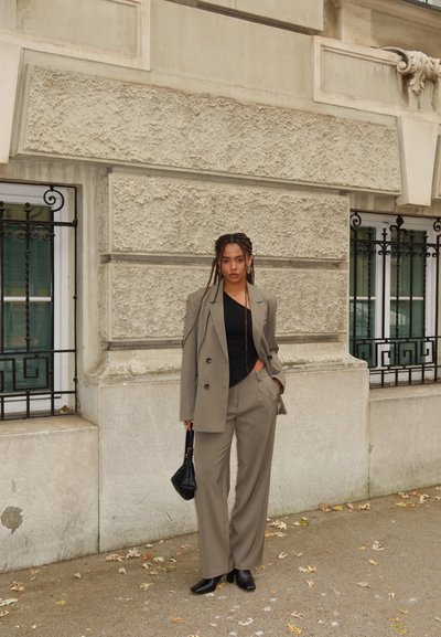 Blazer gris a medida y pantalones de pierna ancha, combinados con un top negro y bolso. Tela suave con textura sutil, ambientados en un fondo urbano.