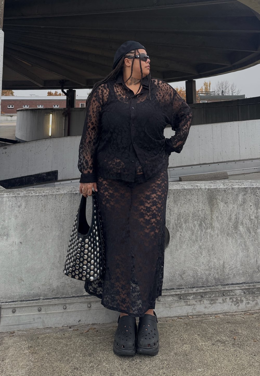 Čierna čipkovaná košeľa so zapínaním na gombíky a zodpovedajúca dlhá sukňa s kvetinovým vzorom. Doplnky tvoria čierna taška s cvokmi a šľapky.