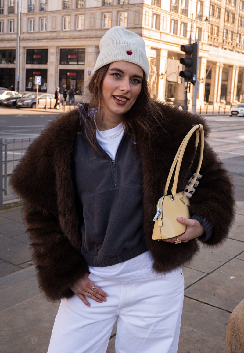 Brown faux fur jacket, grey zip-up hoodie, white t-shirt, white trousers, and a yellow crossbody bag with clear handle and silver zip.