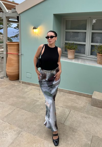 Top negro de canalé sin mangas combinado con una falda larga de satén multicolor con un diseño fluido y una abertura lateral; zapatos negros clásicos.
