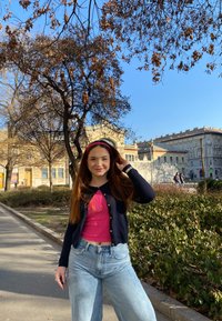 Modella che indossa un cardigan nero sopra una maglietta rosa brillante, abbinato a jeans in denim leggeri blu chiaro a vita alta, in un contesto di parco.