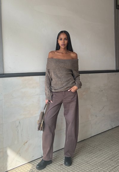 Jersey marrón off-the-shoulder, pantalones marrones holgados, zapatos negros y bolso marrón. Textura suave con detalles acanalados.