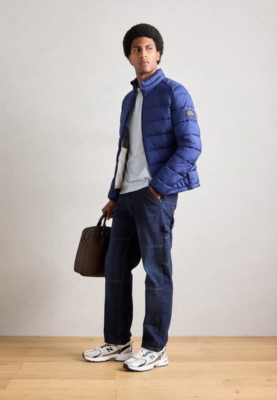 Chaqueta acolchada azul, camisa celeste, pantalones cargo de mezclilla oscura, zapatillas blancas con detalles negros y un bolso de hombro marrón. Texturas lisas visibles.