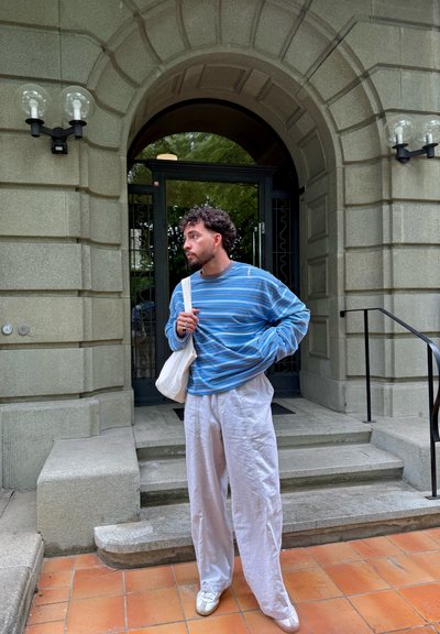 Suéter de rayas de manga larga en azul y blanco, combinado con pantalones blancos de lino sueltos y zapatillas crema. Bolsa tipo tote colgada del hombro.