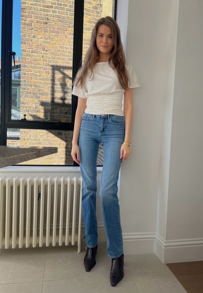 Top blanco de manga corta con detalle fruncido, combinado con unos pantalones vaqueros rectos de color azul claro y botas de tobillo negras con punta afilada.