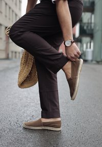 Bruna mocka espadrillos med en flätad jutesula, i kombination med mörka byxor och en vävd väska, accentuerade av ett läderur.