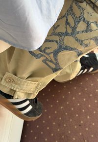 Khaki nadrág kék geometriai mintával, felhajtott szegéllyel, világoskék inggel és fekete cipővel, fehér csíkokkal egy mintás felületen.