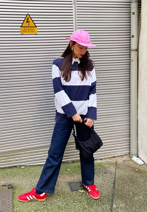 Polo de manga larga a rayas en azul marino y blanco, combinado con pantalones de mezclilla oscuros y zapatillas rojas con rayas blancas. Bolsa tote negra.