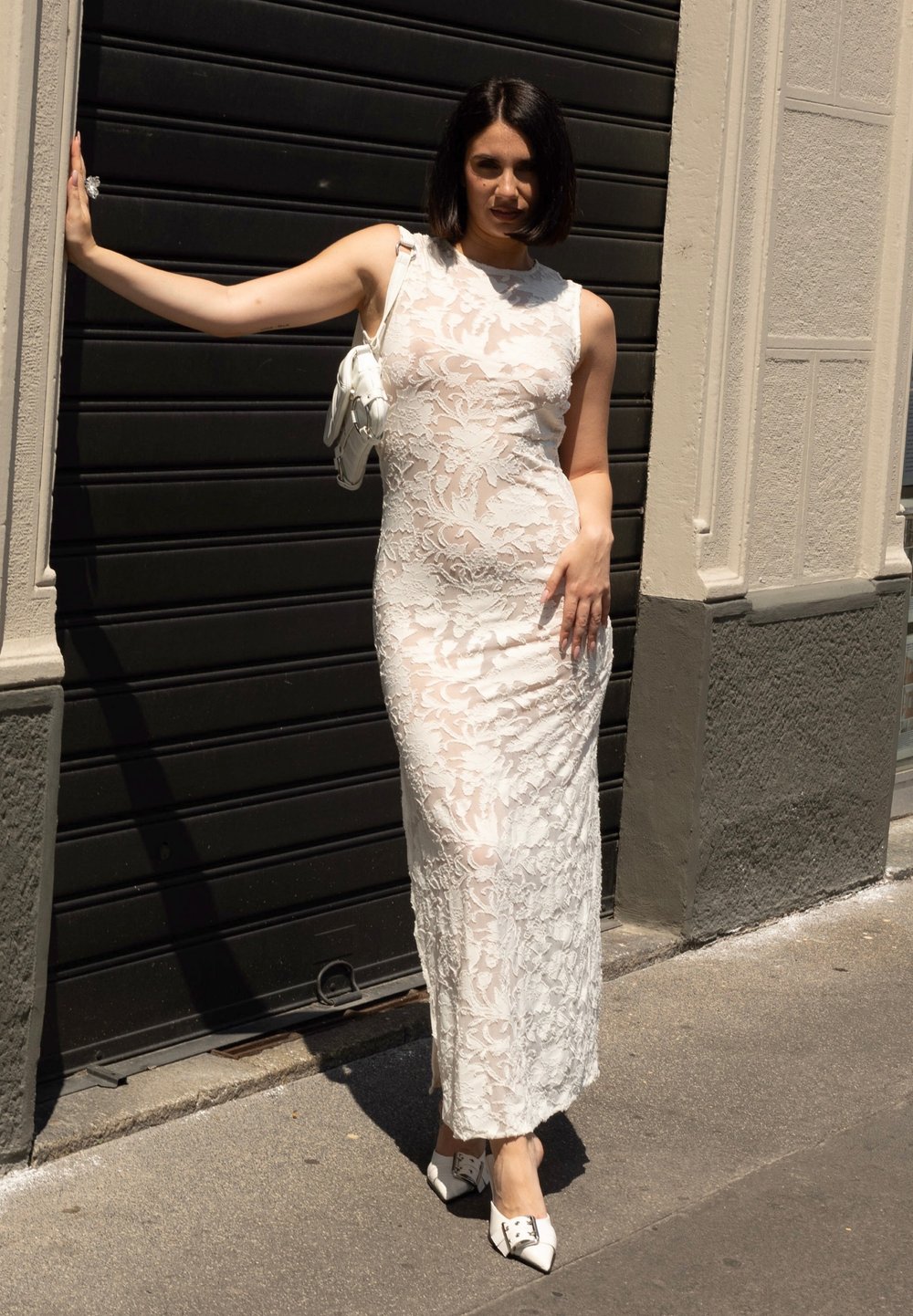 Biała koronkowa sukienka z kwiatowym wzorem, dopasowany krój i bezrękawnik. W połączeniu z białą torebką i butami na spiczastym obcasie.