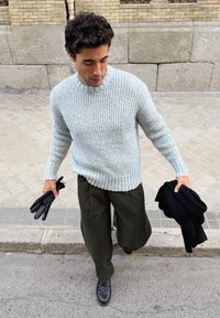 Pull côtelé gris clair, coupe décontractée, avec col rond. Pantalon large vert foncé, gants noirs et écharpe tenue en main. Chaussures noires.