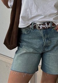 Τζιν σορτσάκια σε ανοιχτό μπλε με ατημέλητες άκρες, συνδ�υασμένα με λευκό μπλουζάκι και πολύχρωμη ζώνη. Ο καστανού χρώματος ώμου τσάντα είναι ορατή.