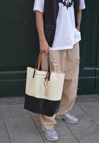 Bolsa de mano con la parte superior en crema y la parte inferior en negro, forma rectangular, con asas de cuero marrón y el logo "MARNI" en el frente.