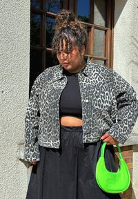 Panterprint denimjakke med knapdetaljer, båret over en sort crop top og lang sort nederdel, parret med en neongrøn taske.