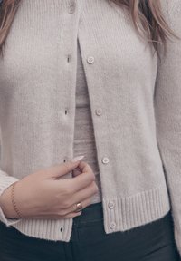 Svetlosivý pletený sveter na gombíky s výstrihom do V a rebrovaným lemom. Má jemnú štruktúru a šesť gombíkov vpredu.