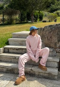 Lichtroze oversized sweatshirt en bijpassende joggers met gathered cuffs, gecombineerd met bruine instappers, zittend op stenen trappen.
